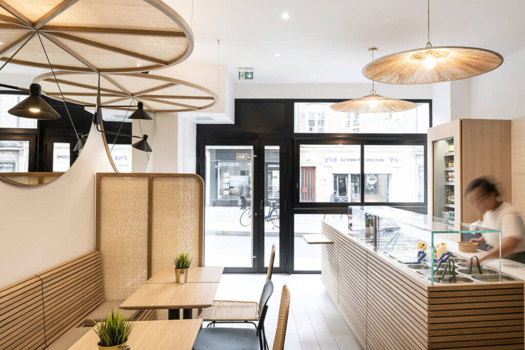 Salle lumineuse d'un restaurant de poké bowl avec banquette, tables en bois et comptoir de composition vitré