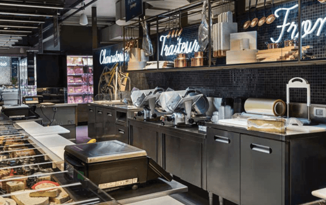 Meuble arrière inox d'un comptoir traiteur avec trancheurs alignés sous une crédence en mosaïque noire