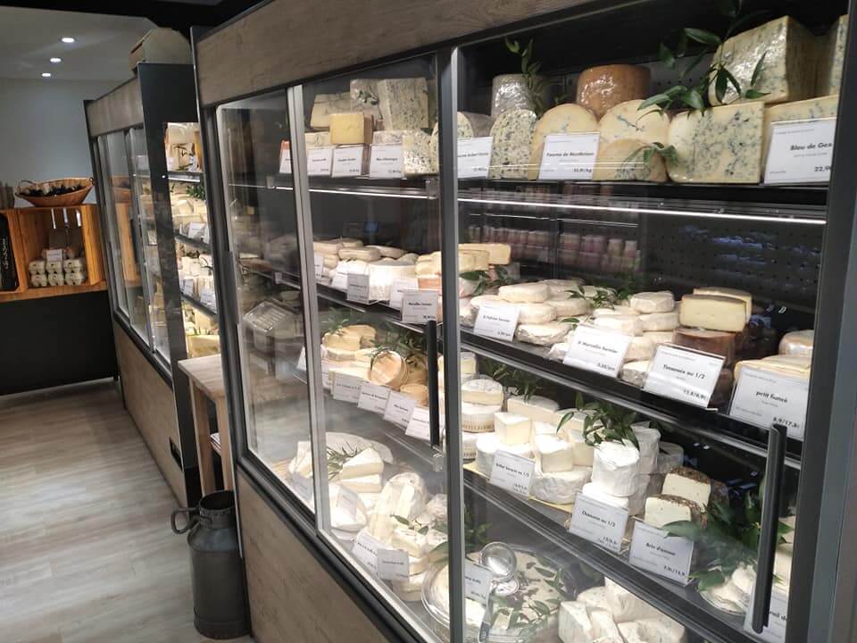 Vitrines murales réfrigérées à portes vitrées garnies de fromages étiquetés dans une fromagerie à Nice