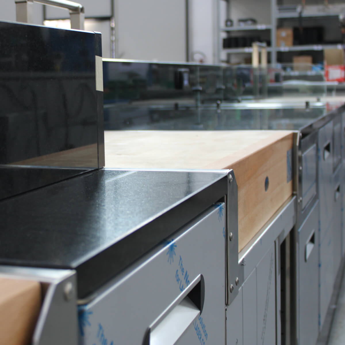 Détail d'un meuble arrière avec dessus granit noir, billot bois et portes inox en atelier