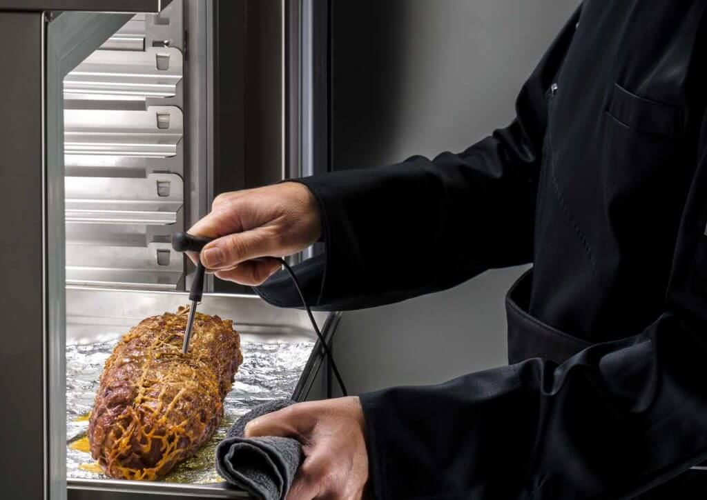 Cuisinier contrôlant à la sonde à cœur la température d'un rôti dans une cellule de refroidissement