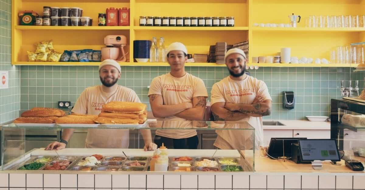 L'équipe de Mitch's derrière le comptoir à sandwichs et ses bacs de garnitures
