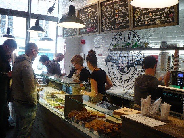 Bagel shop : équipe en préparation derrière le comptoir vitré, clients en commande