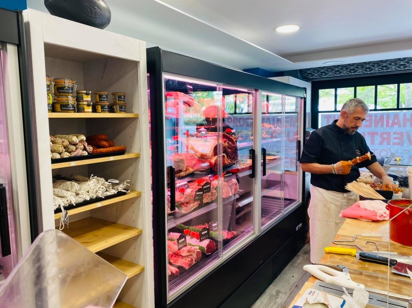 Artisan boucher préparant la viande devant une murale réfrigérée à portes vitrées