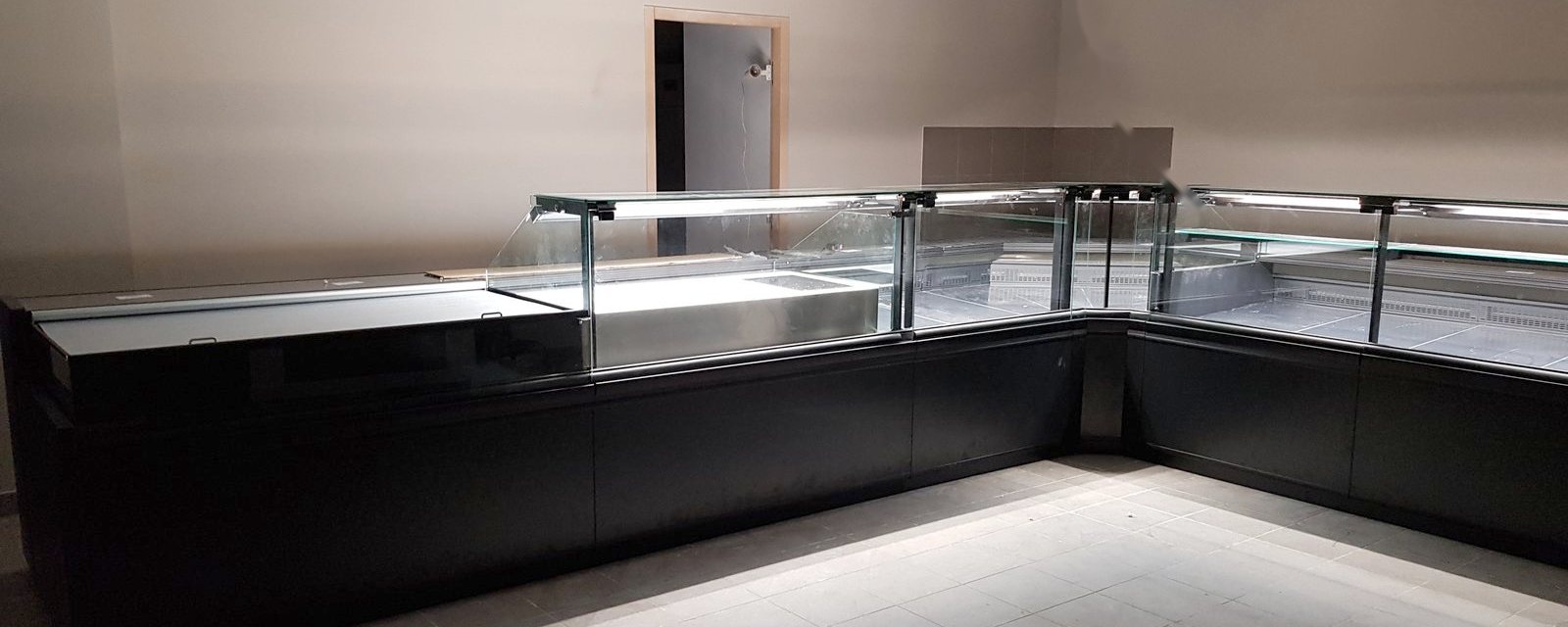 Local de boucherie en travaux avec comptoirs réfrigérés en angle déjà installés avant l'ouverture