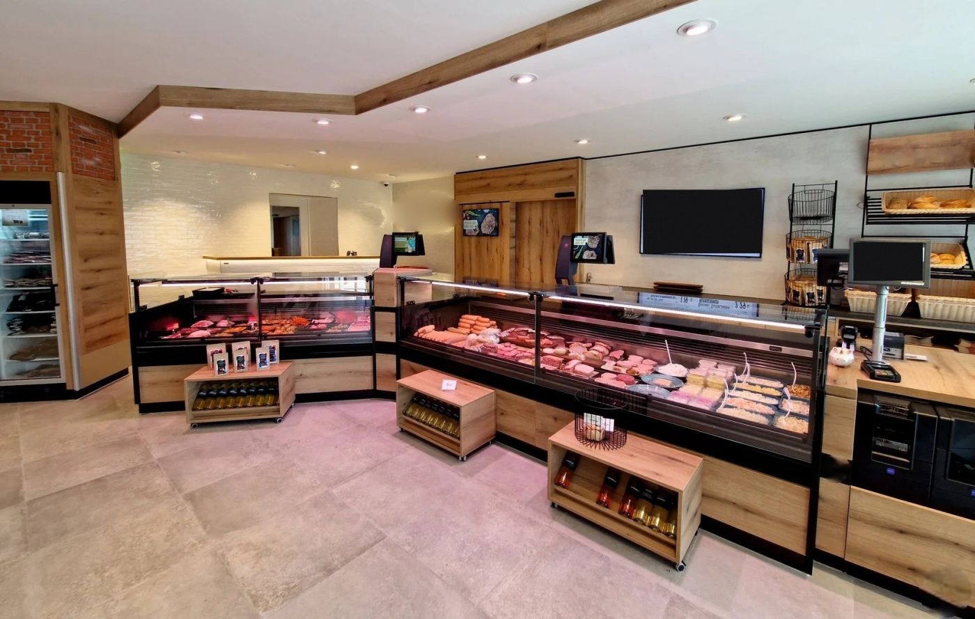 Boucherie-traiteur traditionnelle en décor bois avec comptoirs réfrigérés en angle, viandes à la coupe et rayon traiteur