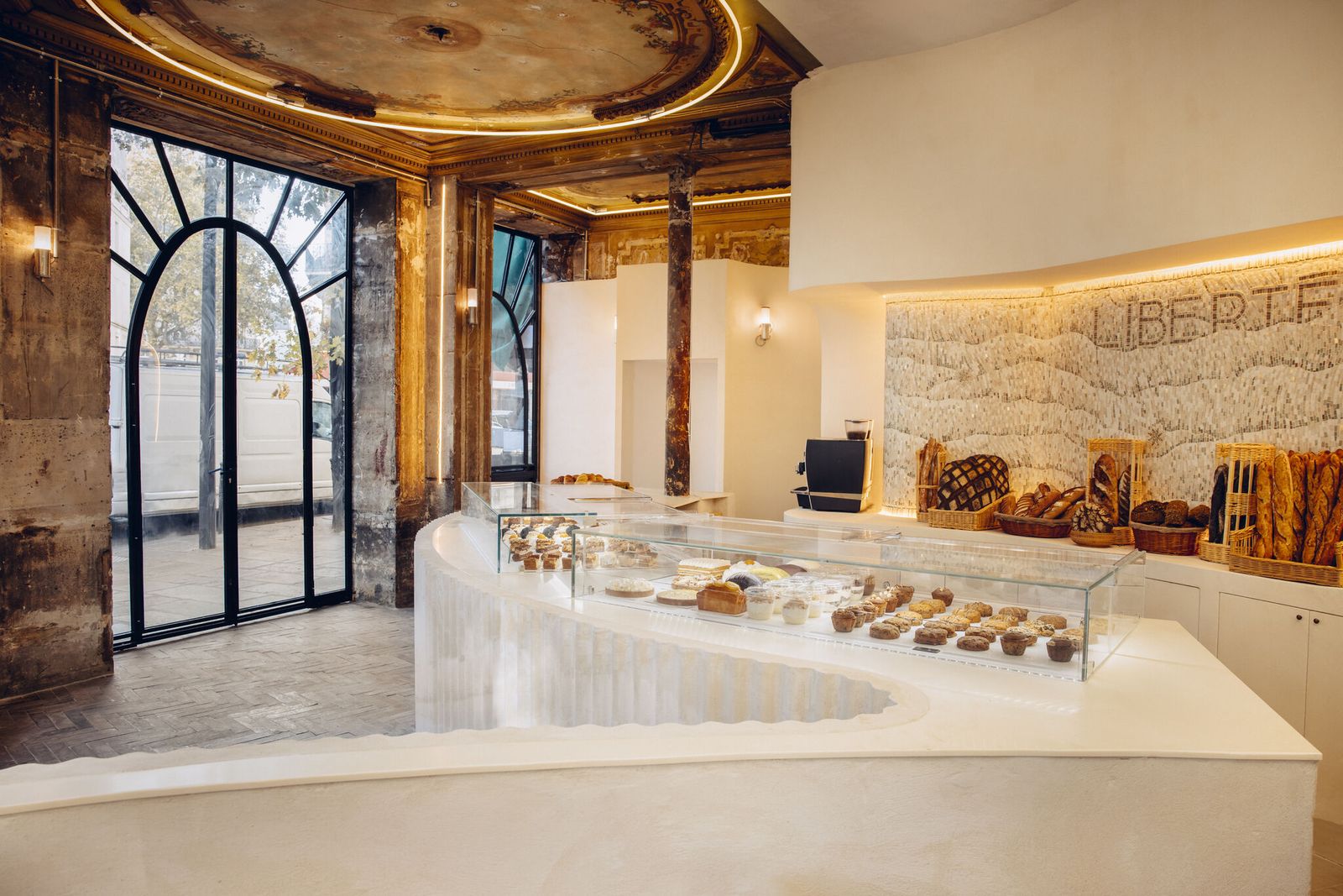 Boulangerie-pâtisserie parisienne avec comptoir courbe blanc, vitrines en verre et viennoiseries, plafond peint restauré