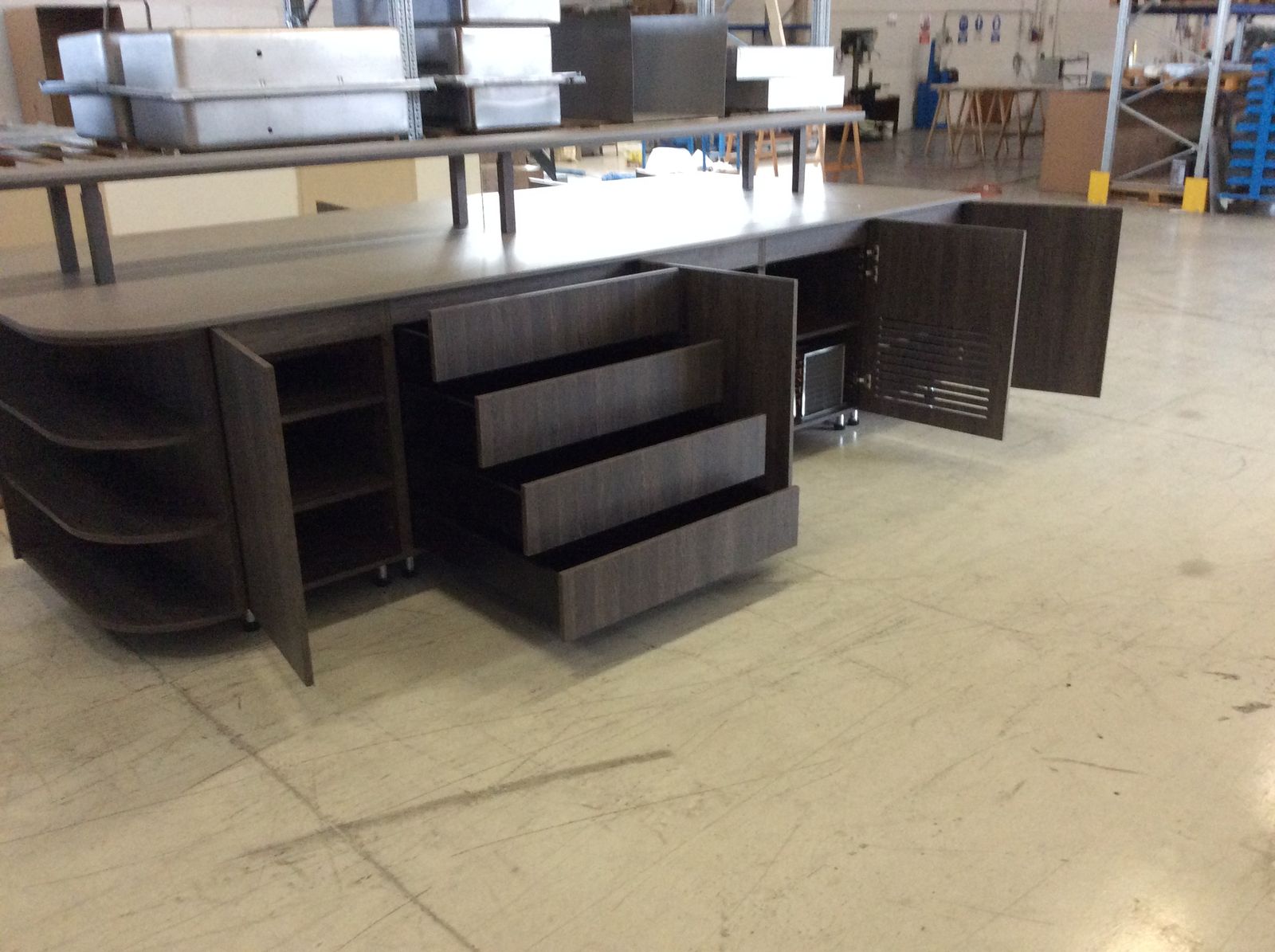 Buffet sur mesure habillé de bois foncé en atelier, portes et tiroirs ouverts sur les compartiments techniques