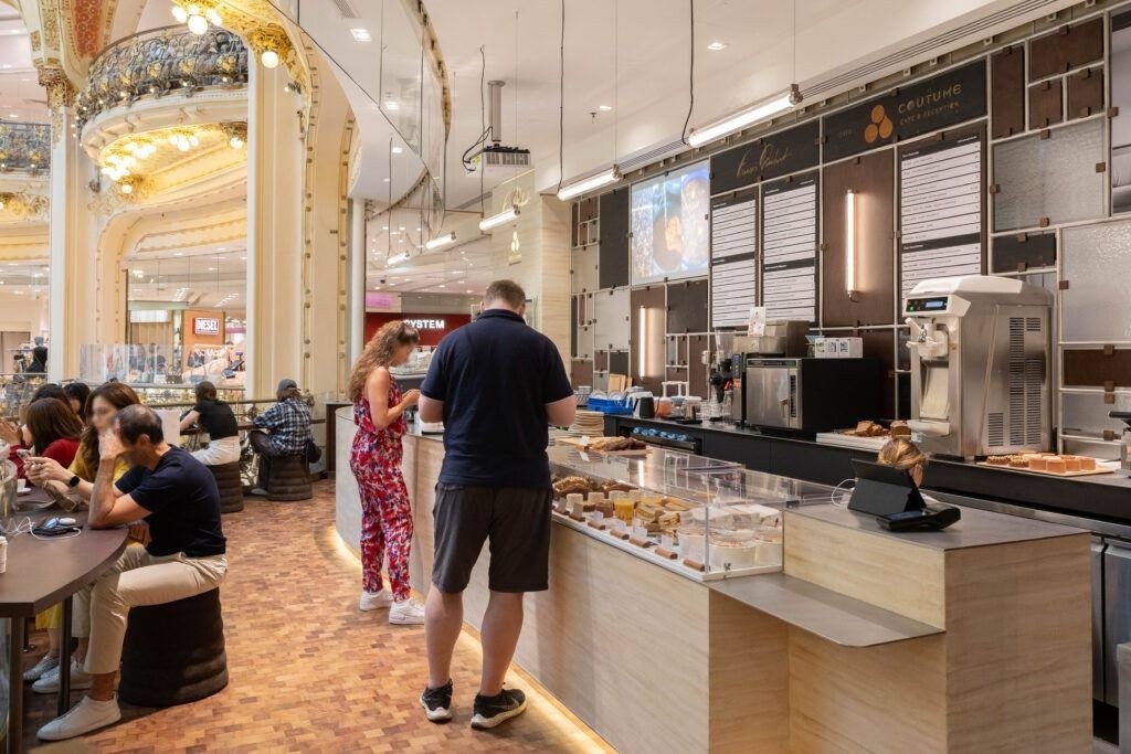 Agencement de coffee shop : coffee shop dans un grand magasin parisien : long comptoir bois, vitrines à pâtisseries et clients attablés