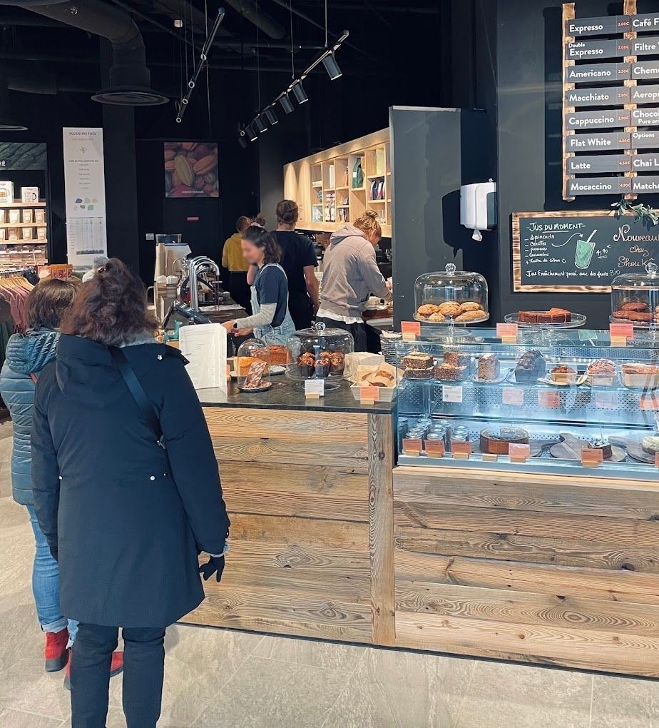 Comptoir de coffee shop en bois brut avec vitrine à pâtisseries et barista en service à Annecy