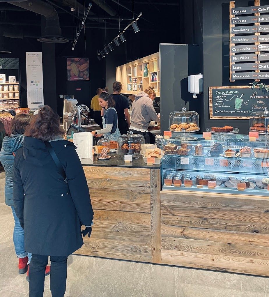 Comptoir de coffee shop en bois brut avec vitrine à pâtisseries et barista en service à Annecy