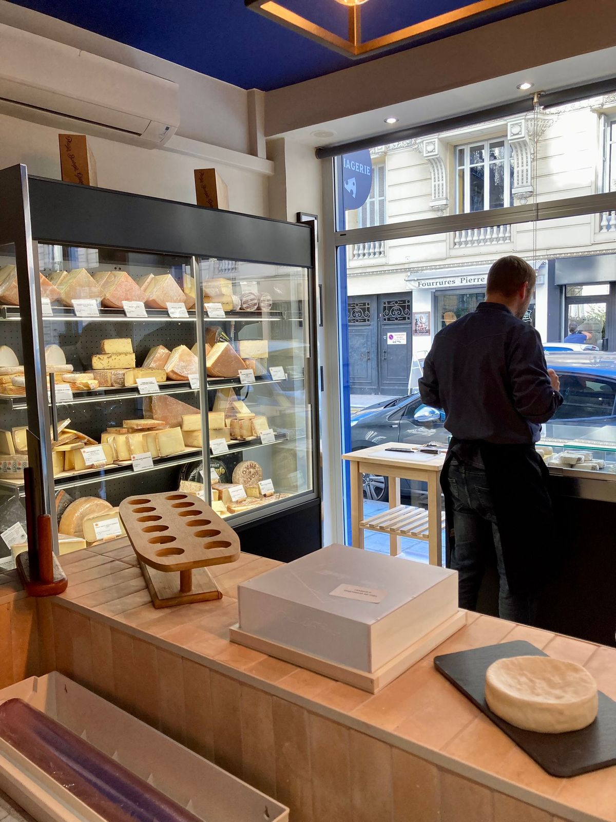 Fromager derrière son comptoir de coupe en bois, murale réfrigérée à fromages en arrière-plan