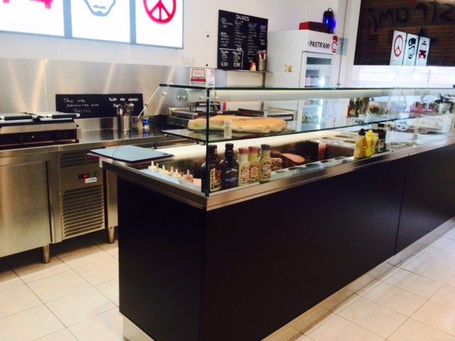Comptoir de sandwichs chauds avec vitrage, façade noire et tables réfrigérées à l’arrière