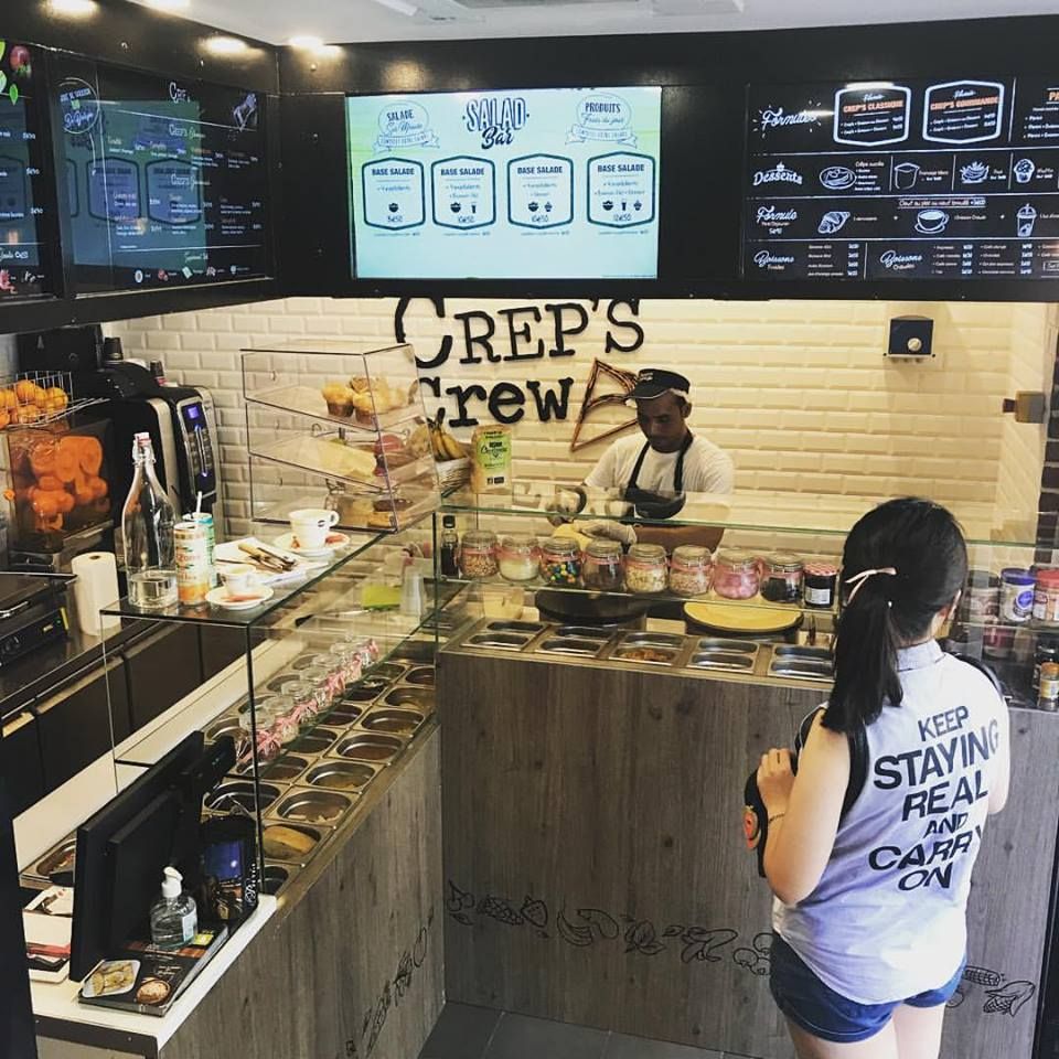 Crêperie à Paris : crêpier au travail derrière un comptoir de garnitures sous vitrage, cliente en commande