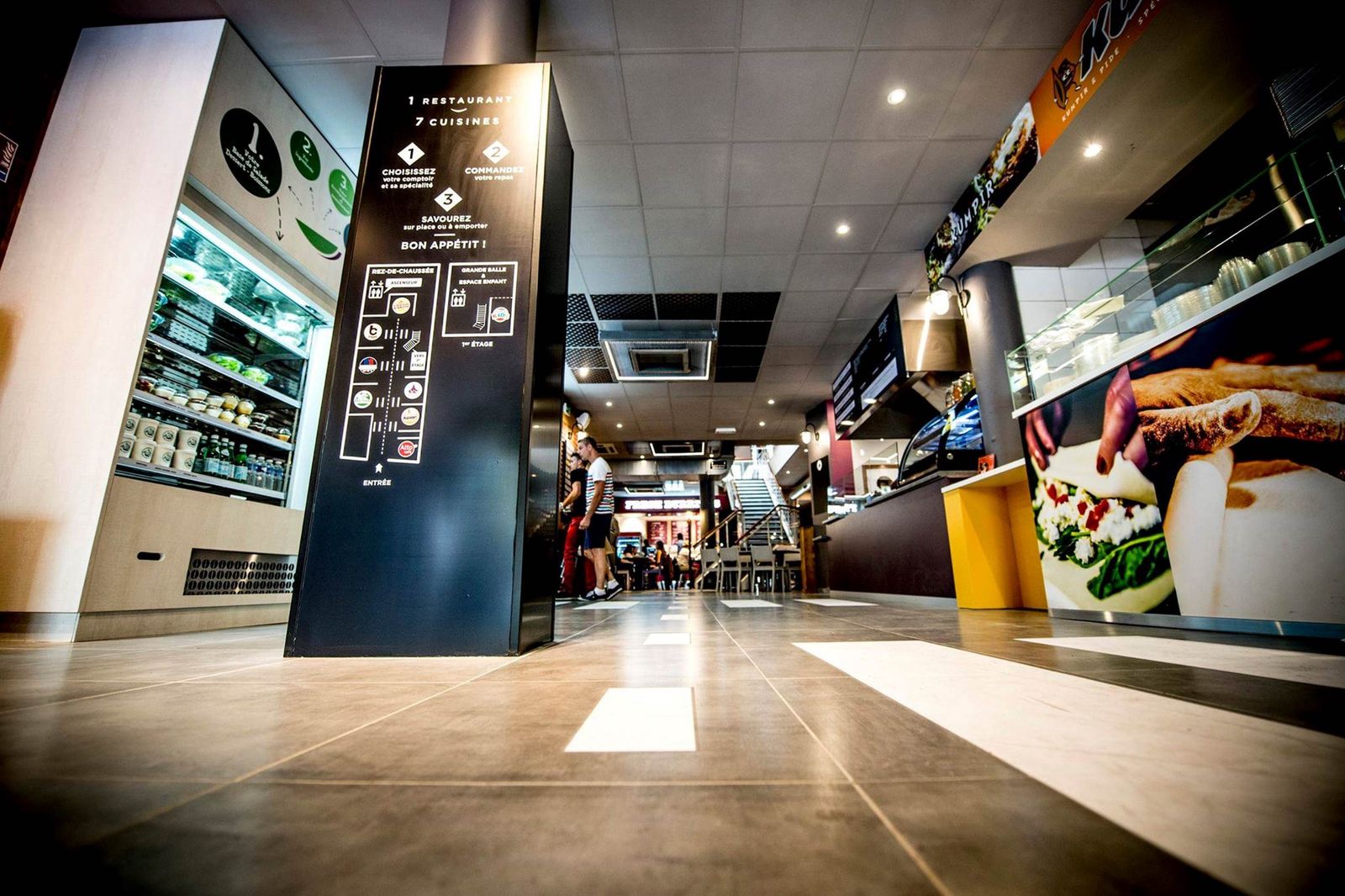 Allée d’un food court avec murale réfrigérée libre-service et stands de restauration à Reims