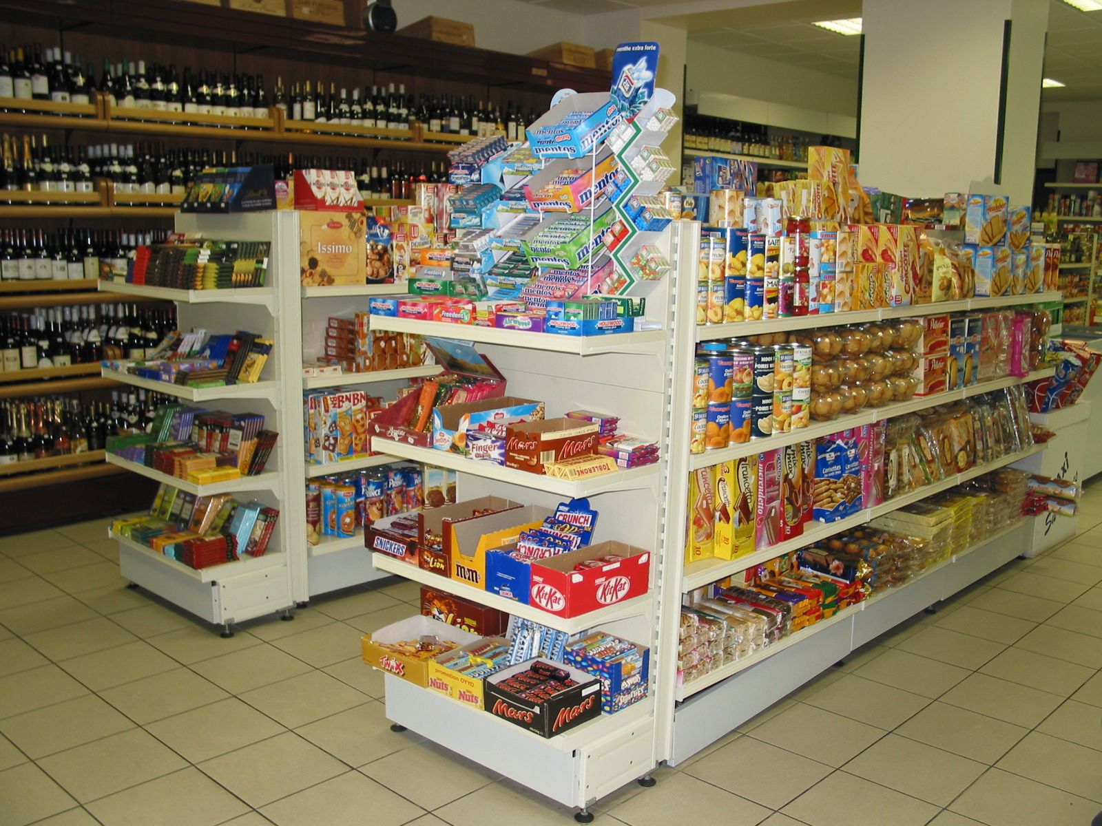 Gondoles de supérette garnies d’épicerie et de confiserie, rayon cave en arrière-plan