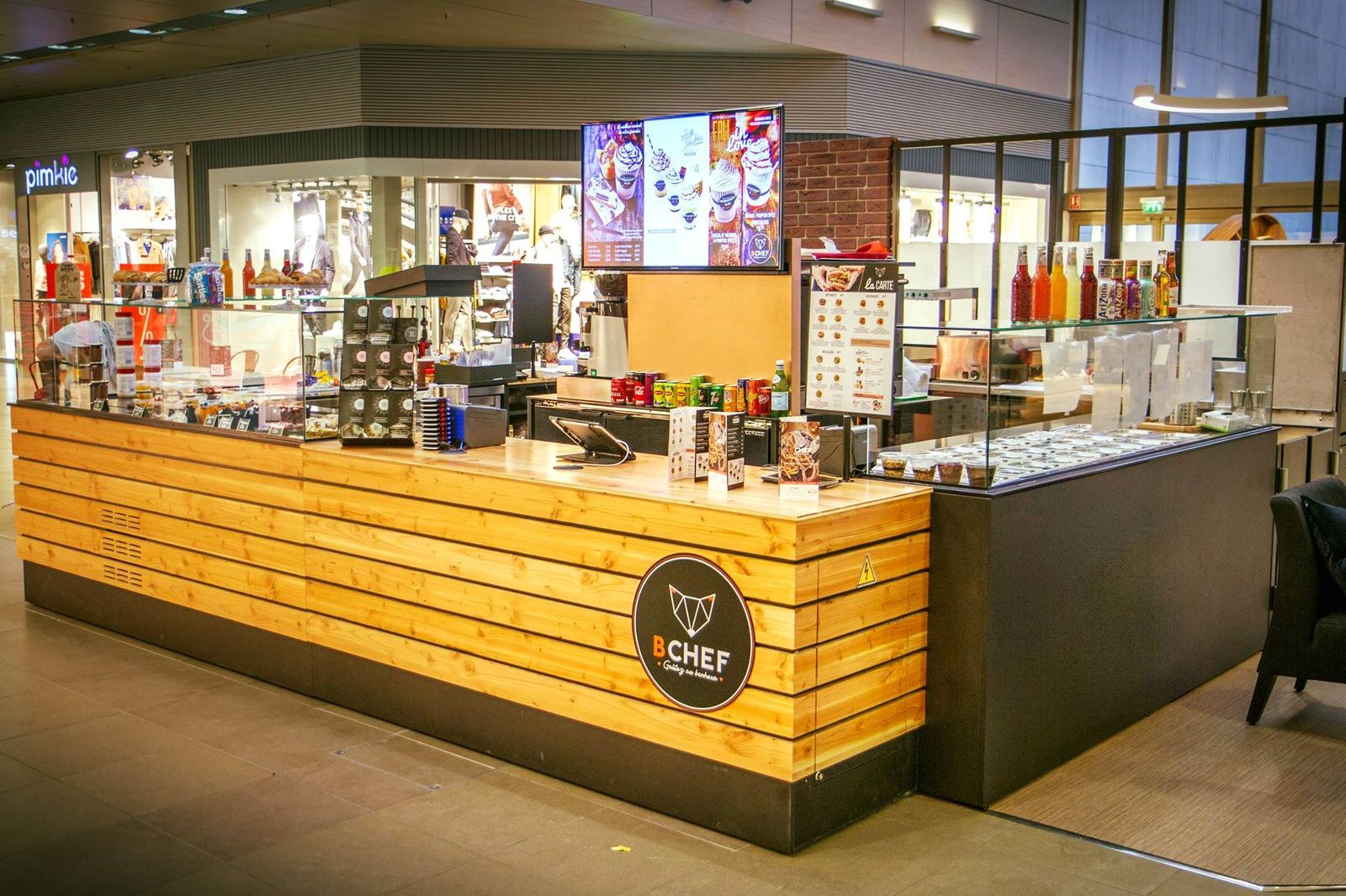 Kiosque de bagels et burgers en galerie commerciale avec comptoir habillé de bois et vitrines