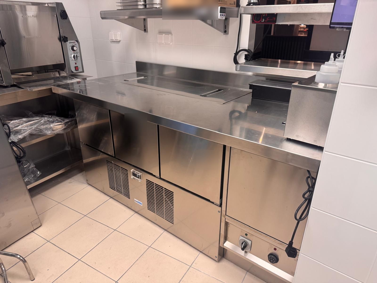 Arrière-comptoir de préparation en inox avec tables réfrigérées et rangements dans une boulangerie