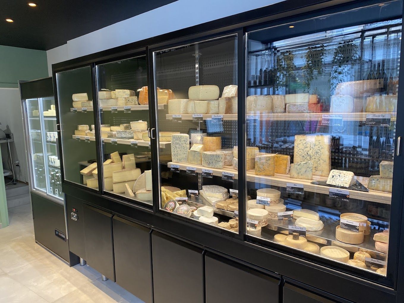 Murale réfrigérée noire à portes vitrées garnie de meules et de fromages à la coupe