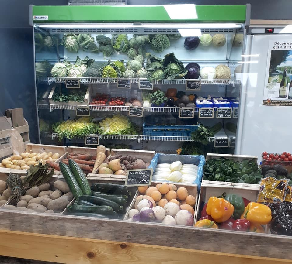 Murale réfrigérée de primeur garnie de choux, salades et légumes, cagettes de fruits et légumes au premier plan