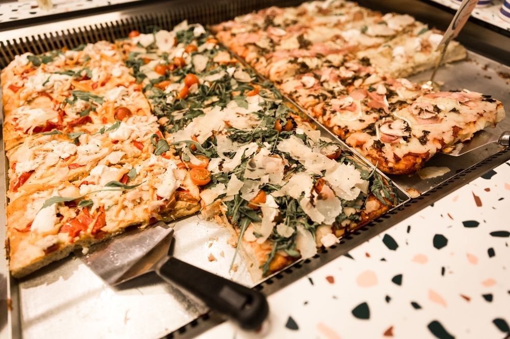 Plaques de pizza al taglio découpées dans la vitrine d’une pizzeria parisienne
