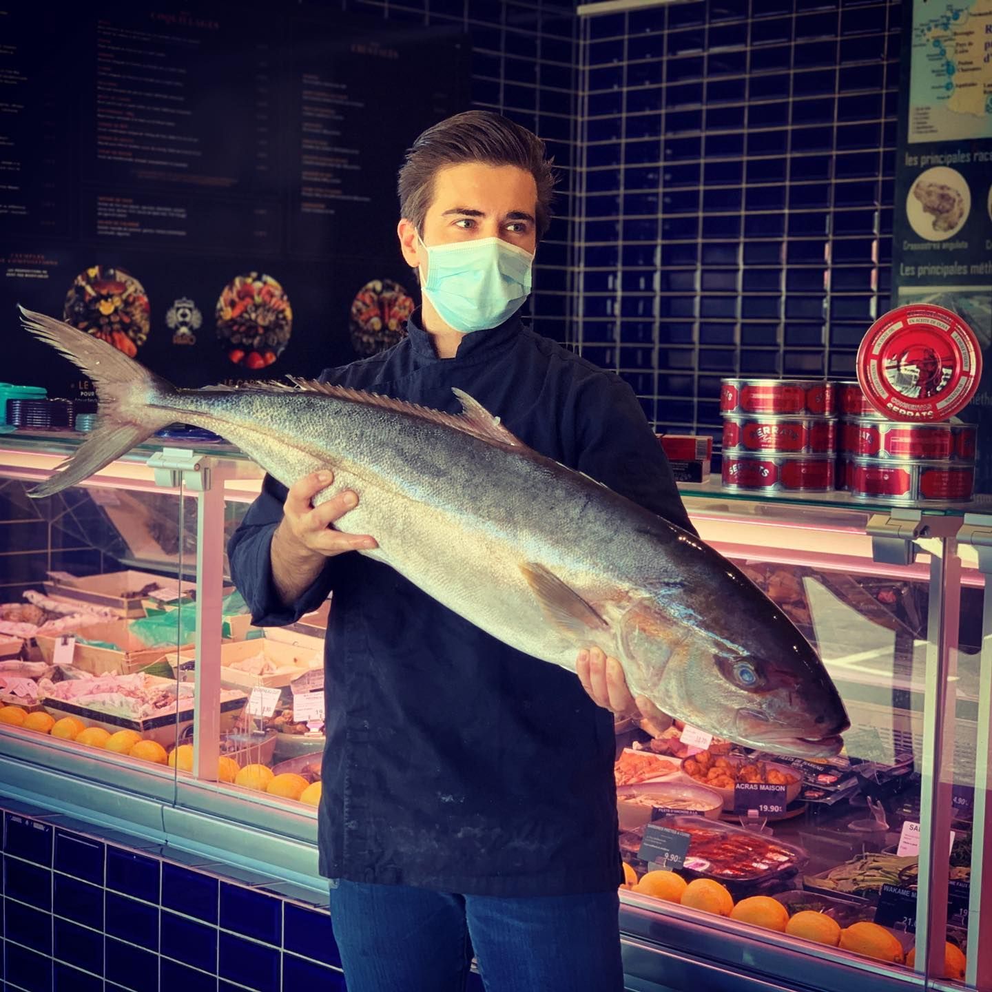 Poissonnier présentant un poisson entier devant ses vitrines réfrigérées à Aix-en-Provence