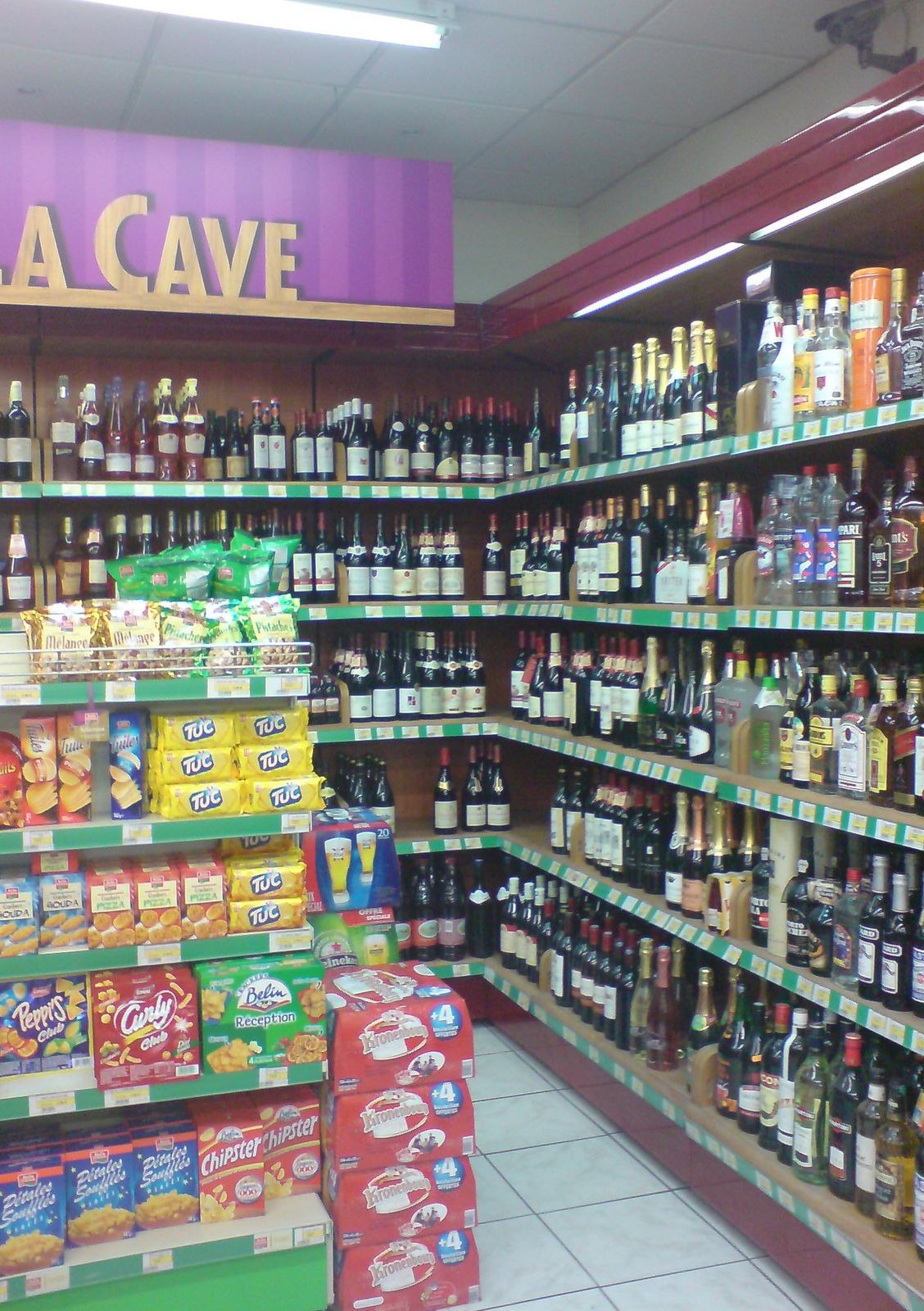 Rayon cave d’une supérette avec étagères murales de vins et spiritueux et gondole d’épicerie