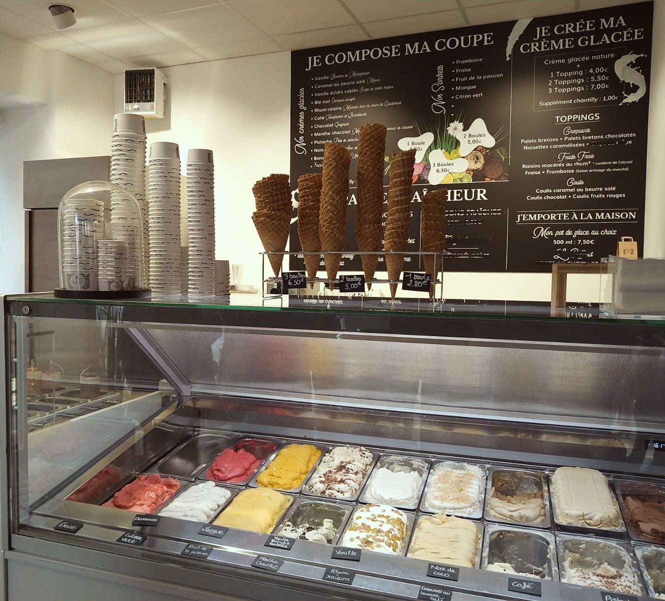 Vitrine à glaces en bacs avec menu de coupes et toppings dans un glacier fermier