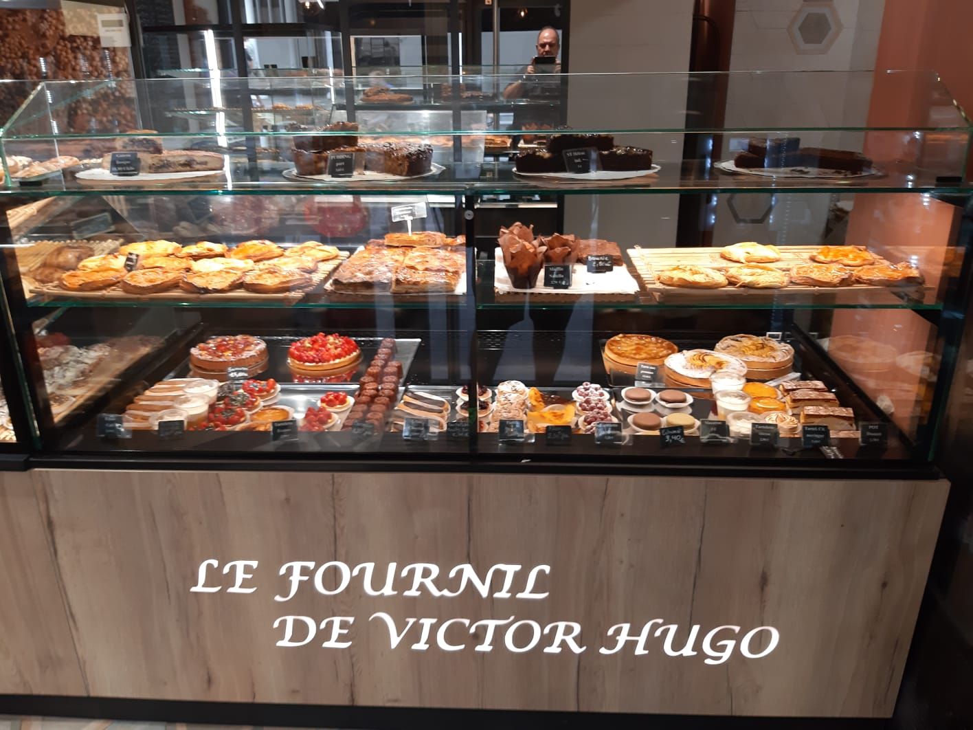 Vitrine réfrigérée sur deux niveaux garnie de tartes, quiches et pâtisseries, façade bois au nom de la boulangerie