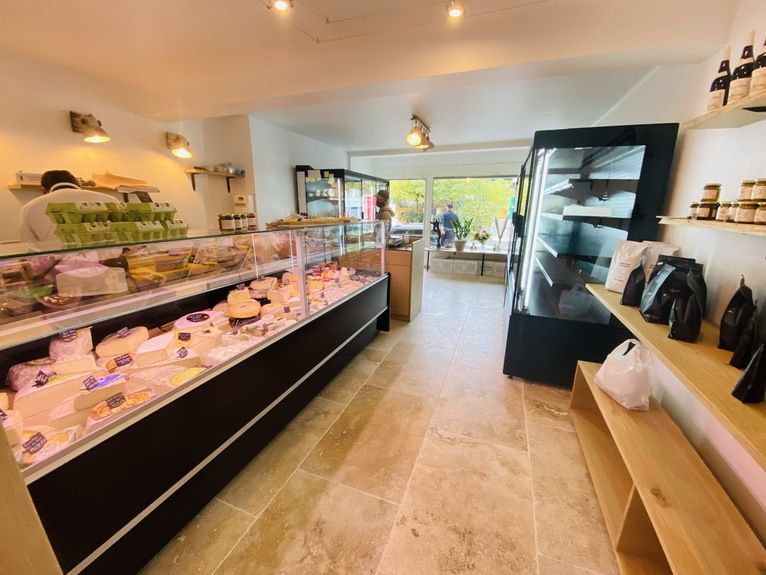 Vitrine réfrigérée de comptoir à façade noire garnie de fromages dans une crémerie lumineuse