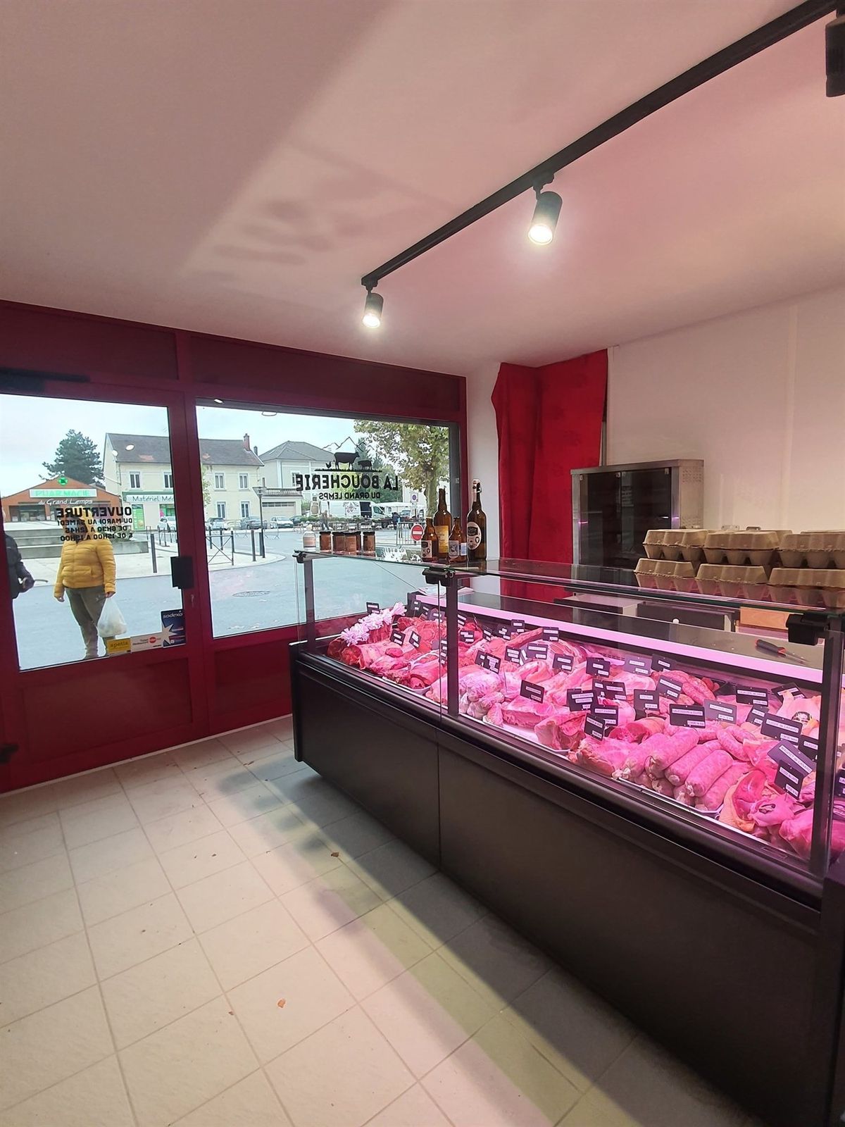 Vitrine réfrigérée de boucherie à façade noire garnie de viandes, éclairage rose