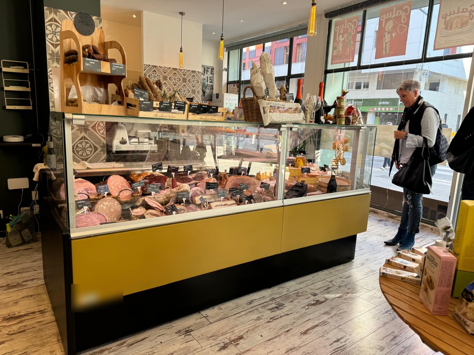 Vitrine réfrigérée de trattoria garnie de charcuteries italiennes et de fromages, façade jaune moutarde