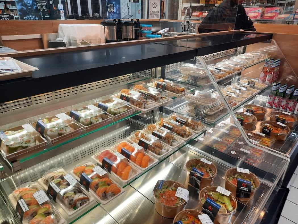 Vitrine de kiosque à sushis présentant plateaux, bowls et barquettes sous vitrage