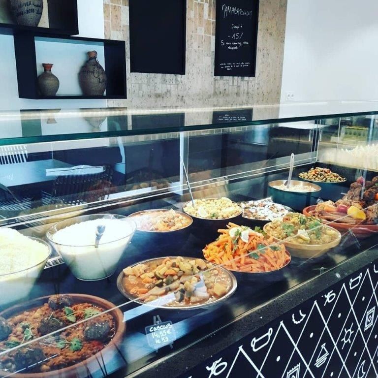 Vitrine de traiteur oriental présentant plats de couscous, tajines et salades sur un comptoir noir à motifs